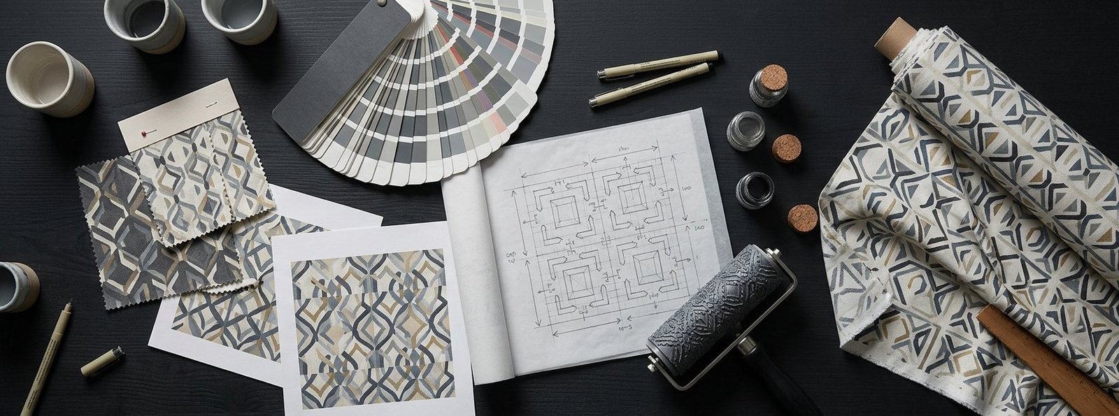 Repeat pattern swatches, a colour chip fan and a printed textile roll on a surface design worktable
