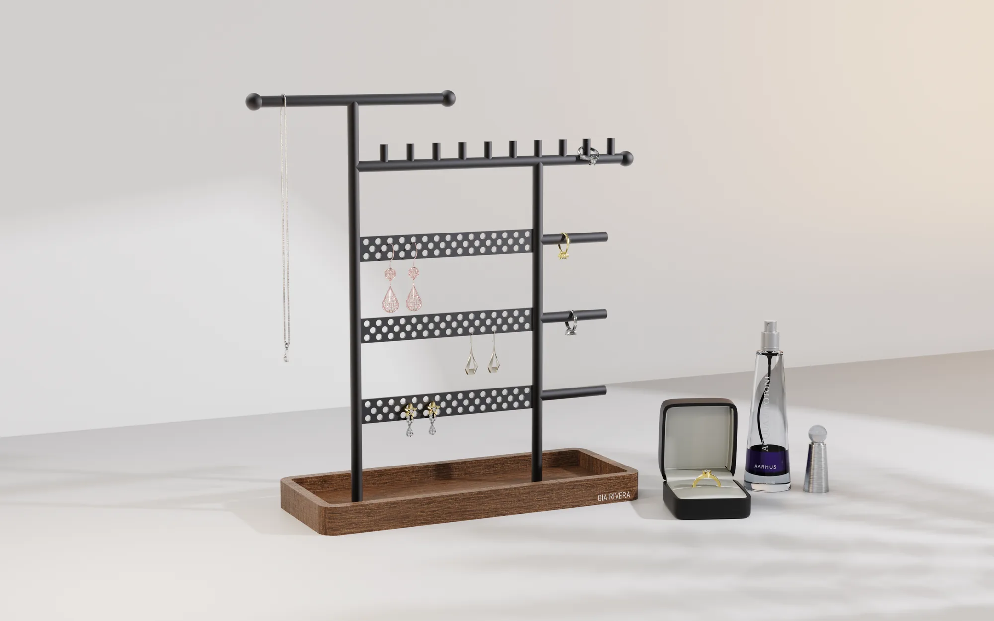 Matte black steel Gia Rivera jewellery stand styled with a necklace, rings and earrings against a soft studio backdrop, a ring box and scent bottle beside it.